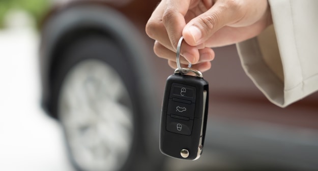 main tenant une clé de voiture avec une voiture en fond