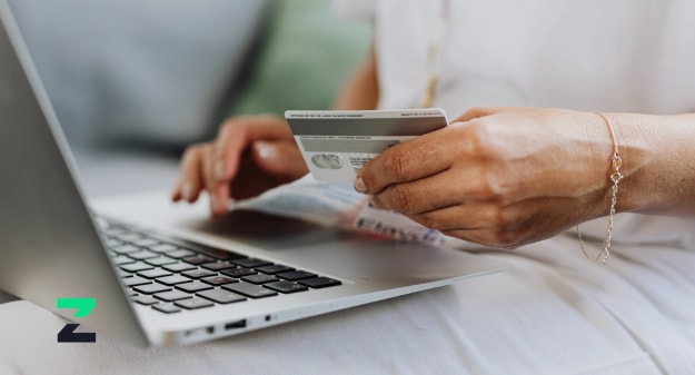 personne avec carte bancaire en mains face à un ordinateur portable